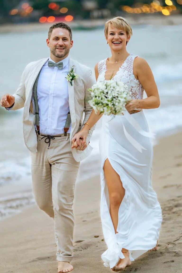 A couple walking hand in hand along the shoreline, the bride in a split-front white gown, Koh Lanta, Lucida Image