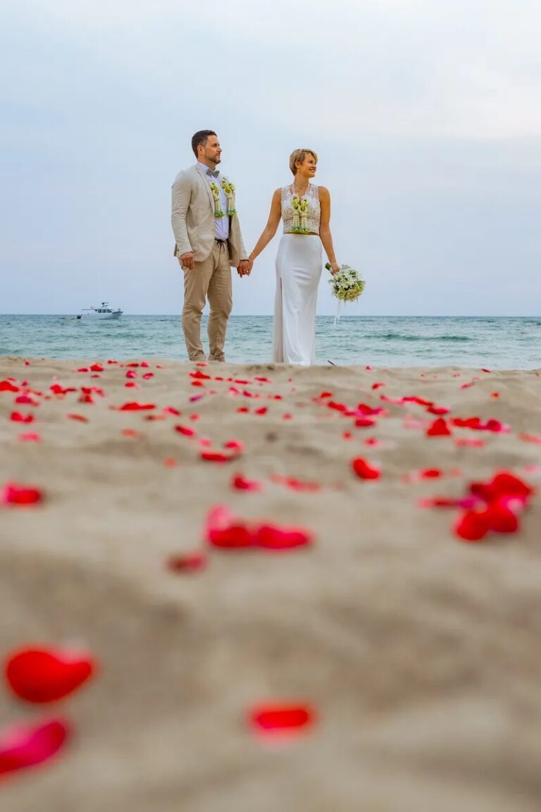 A couple walking towards the camera along a trail of red petals on the sand, Koh Lanta, Lucida Image