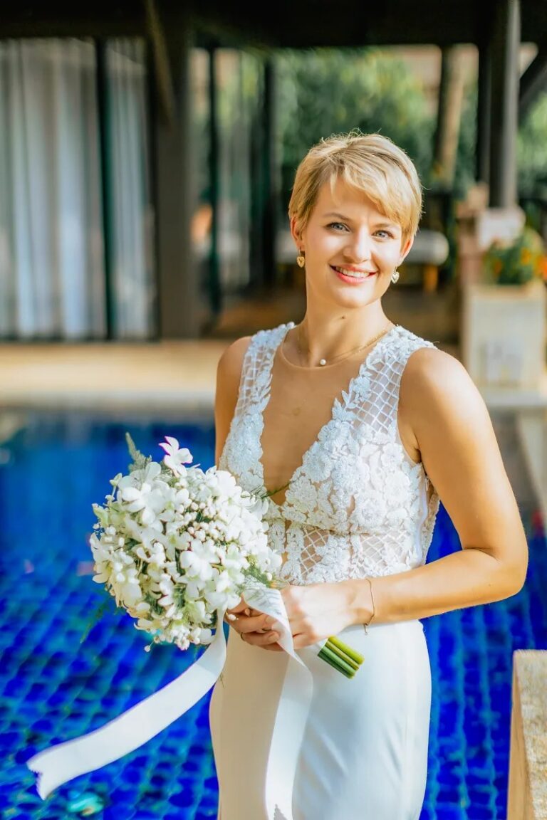 A bride in a white two-piece gown with a white bouquet beside a blue-tiled pool, Koh Lanta, Lucida Image