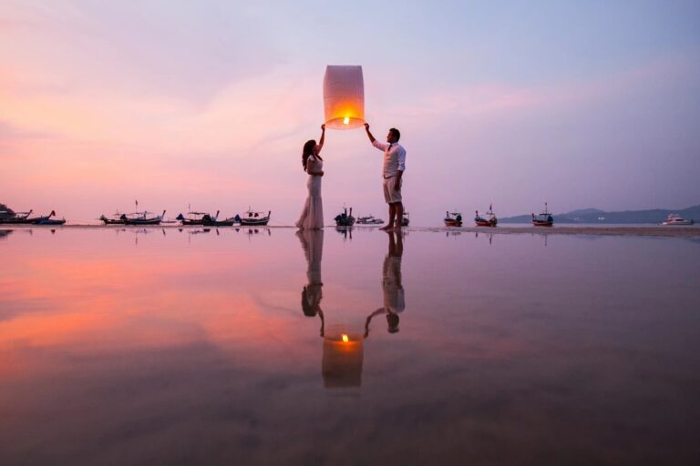 A couple holding a glowing sky lantern against a pink sunset reflected on a tidal flat, Lucida Image
