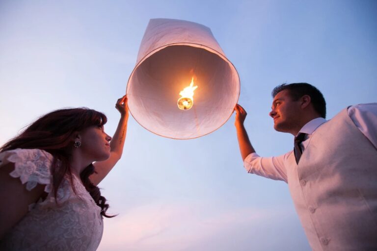 A couple releasing a lit sky lantern against a pale blue sky, Lucida Image