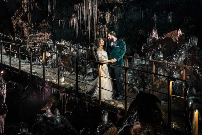 A couple on a lit walkway inside a lava tunnel, with ice formations around them, Luxwedding Iceland