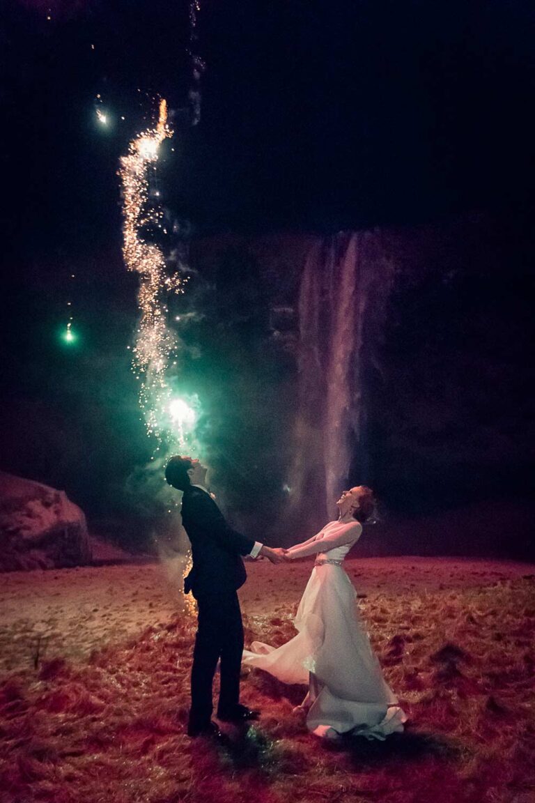 A couple with fireworks in front of a floodlit waterfall on a winter night, Luxwedding Iceland