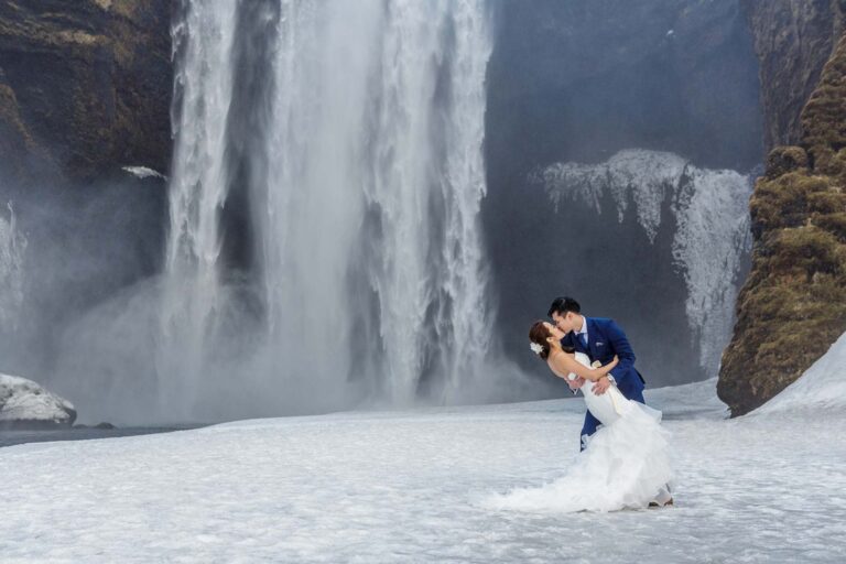 A couple kiss in front of a large waterfall surrounded by snow on the south coast, Luxwedding Iceland
