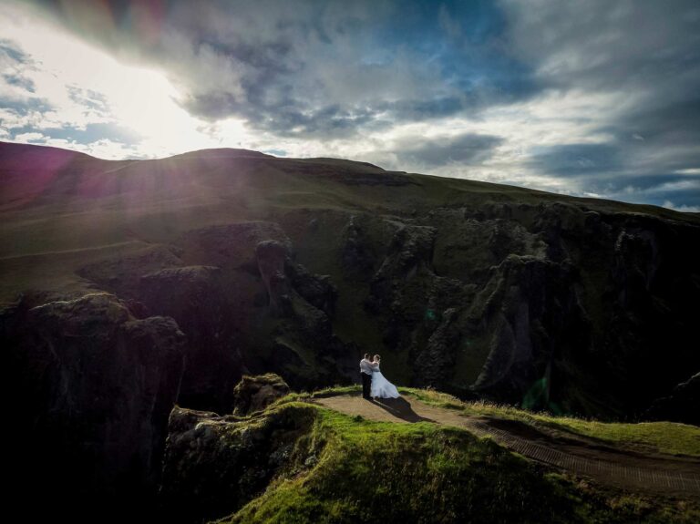 A couple on a grassy ridge above a deep Icelandic canyon at sunset, Luxwedding Iceland