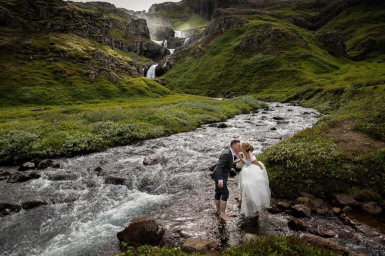 A couple kiss beside a mountain stream in a green highland valley, Luxwedding Iceland