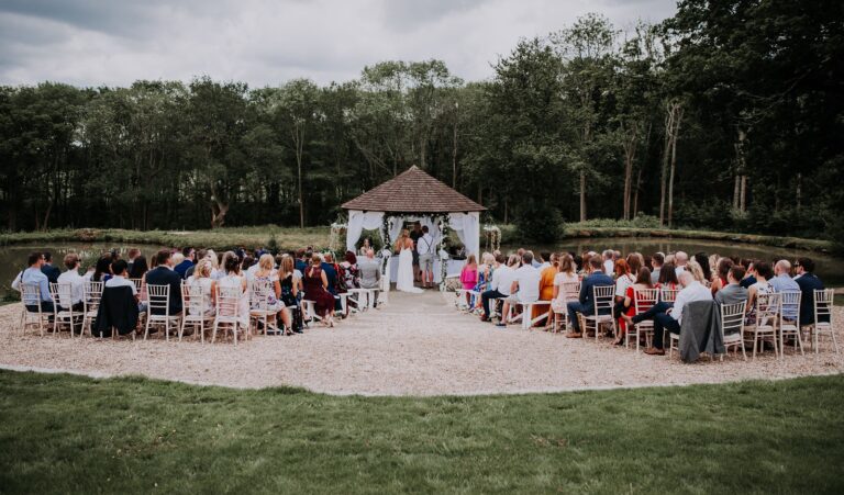An outdoor ceremony in a woodland clearing, guests seated around the couple beneath the trees, Lythe Hill Hotel & Spa
