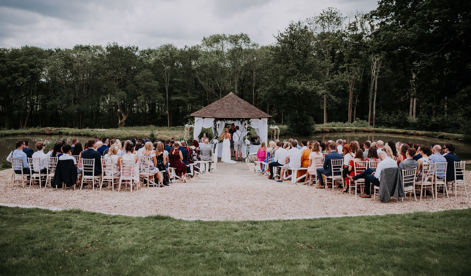 An outdoor ceremony in a woodland clearing, guests seated around the couple beneath the trees, Lythe Hill Hotel & Spa