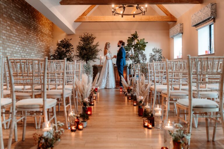 The bride and groom at the head of a candlelit aisle in the beamed Hampton Suite, Lythe Hill Hotel & Spa