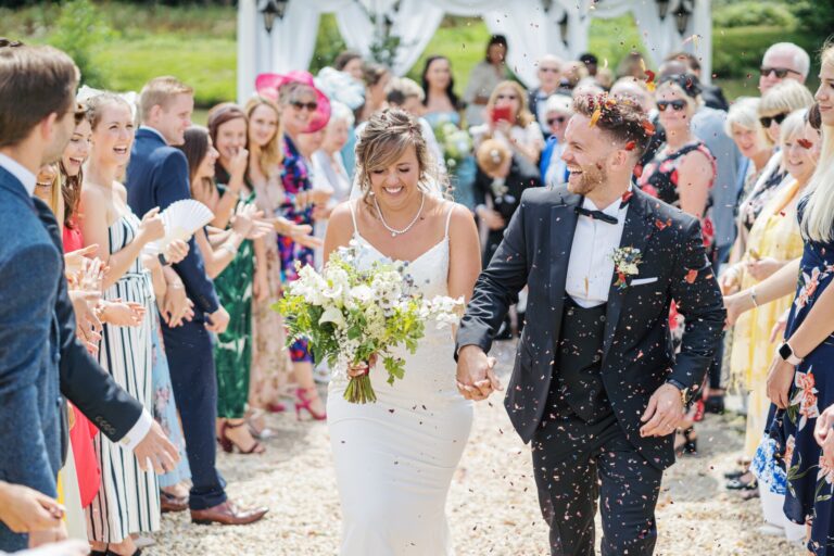 The newlyweds walking through a shower of confetti and their cheering guests, Lythe Hill Hotel & Spa