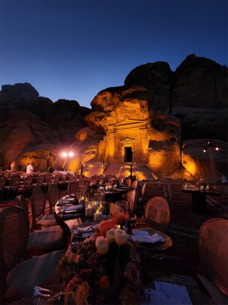 Dusk table setting with florals and the lit facade behind, Mövenpick Resort Petra
