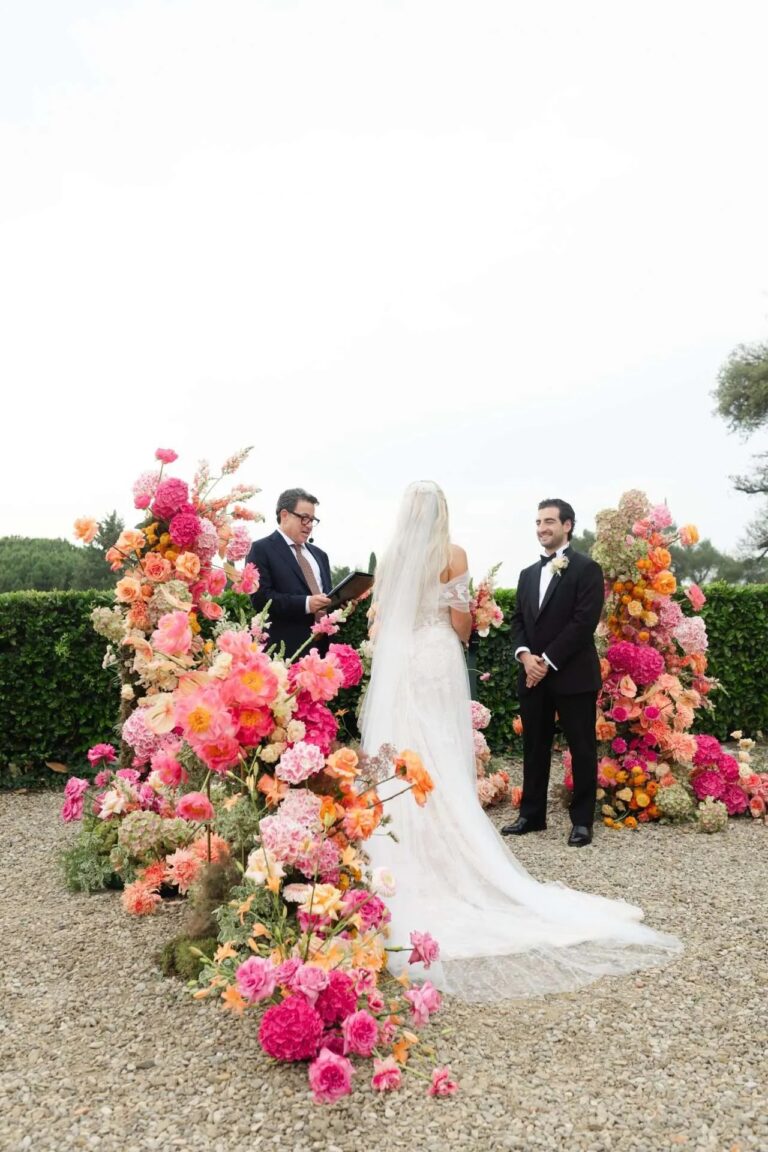 The couple at the altar between two waves of coral and magenta flowers, Magnolia Wedding Planner