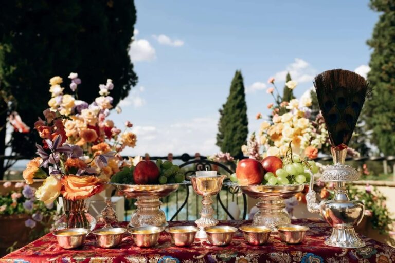 A Nepali ceremony table with brass vessels, fruit and flowers on a red cloth, Chianti, Magnolia Wedding Planner