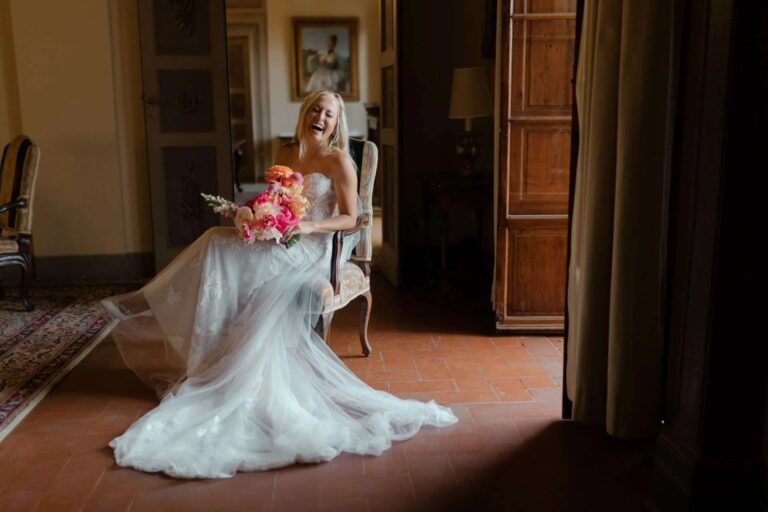 The bride laughing on a chair in a terracotta-floored room, bouquet in her lap, Magnolia Wedding Planner