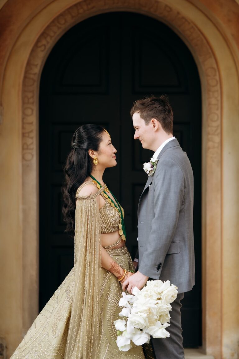 The couple in an arched doorway, a gold lehenga and a grey morning suit, Magnolia Wedding Planner