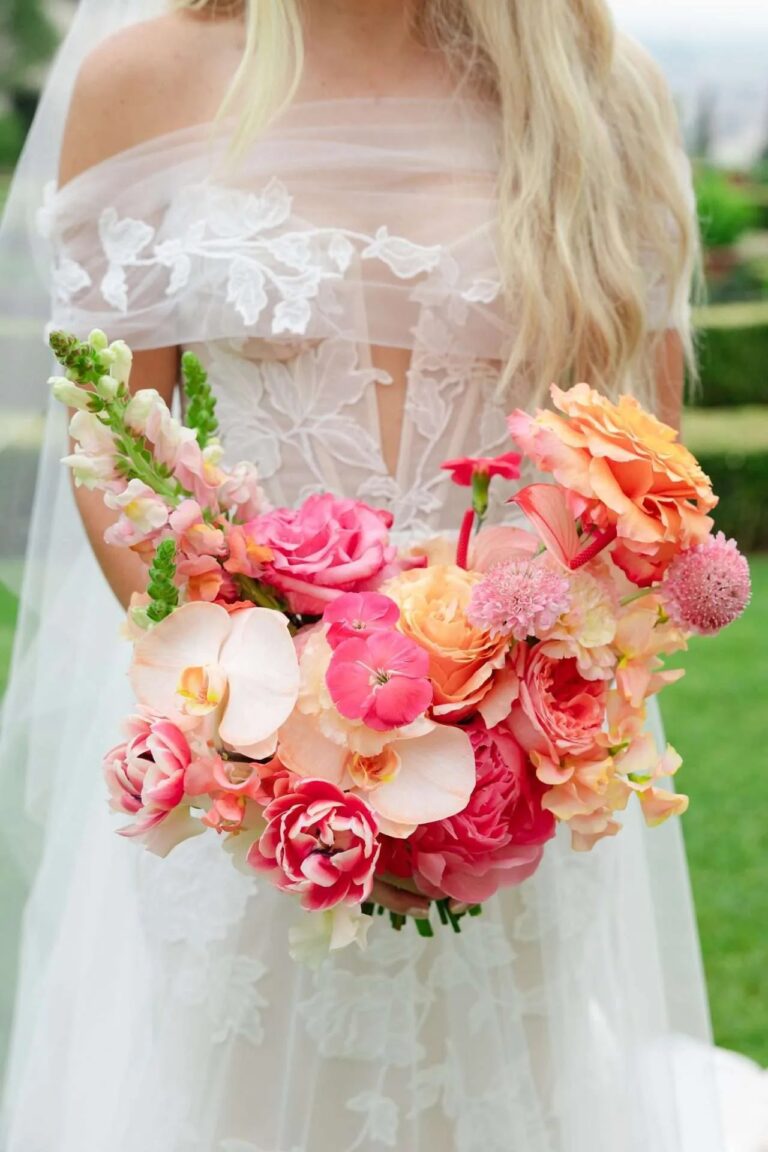Coral roses, ranunculus and orchids held against a sheer lace bodice, Magnolia Wedding Planner