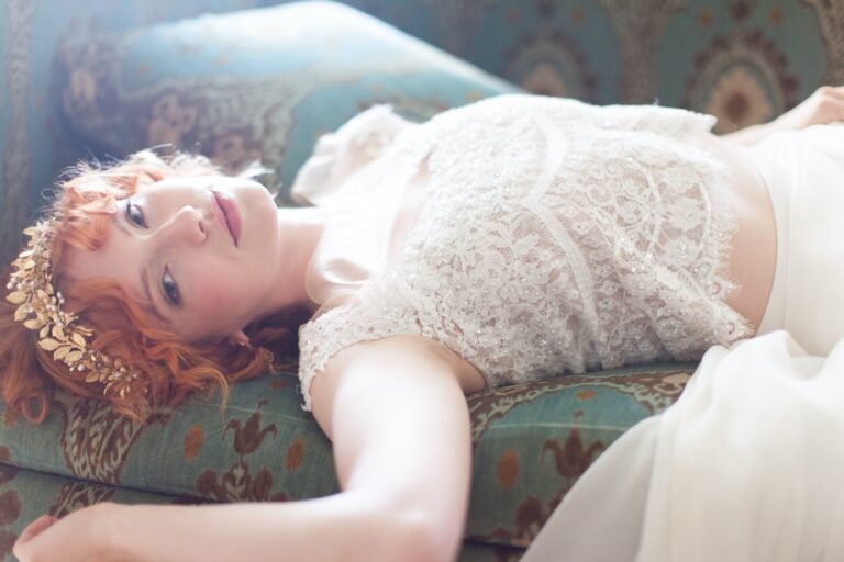 A bride reclining on a vintage sofa in a beaded lace gown, a gold leaf headpiece, Makeup By Becky Flynn