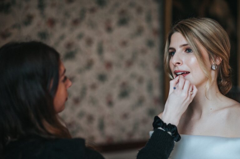 Lip makeup being applied to a bride, a floral wallpaper behind them, Makeup By Becky Flynn