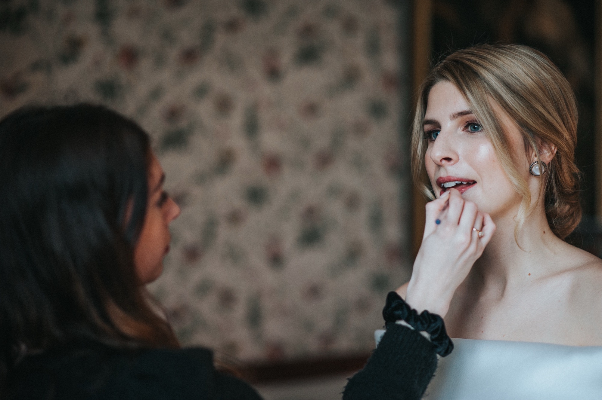 Lip makeup being applied to a bride, a floral wallpaper behind them, Makeup By Becky Flynn