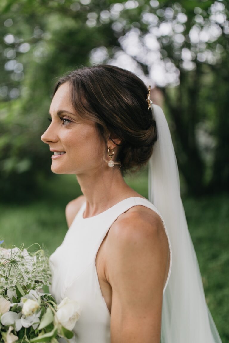 A bride in a veil beneath blossom trees, seen from behind, Makeup By Becky Flynn