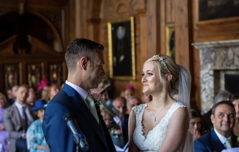A wedding ceremony mid-vow, guests seated either side of a panelled room, Makeup By Mirna