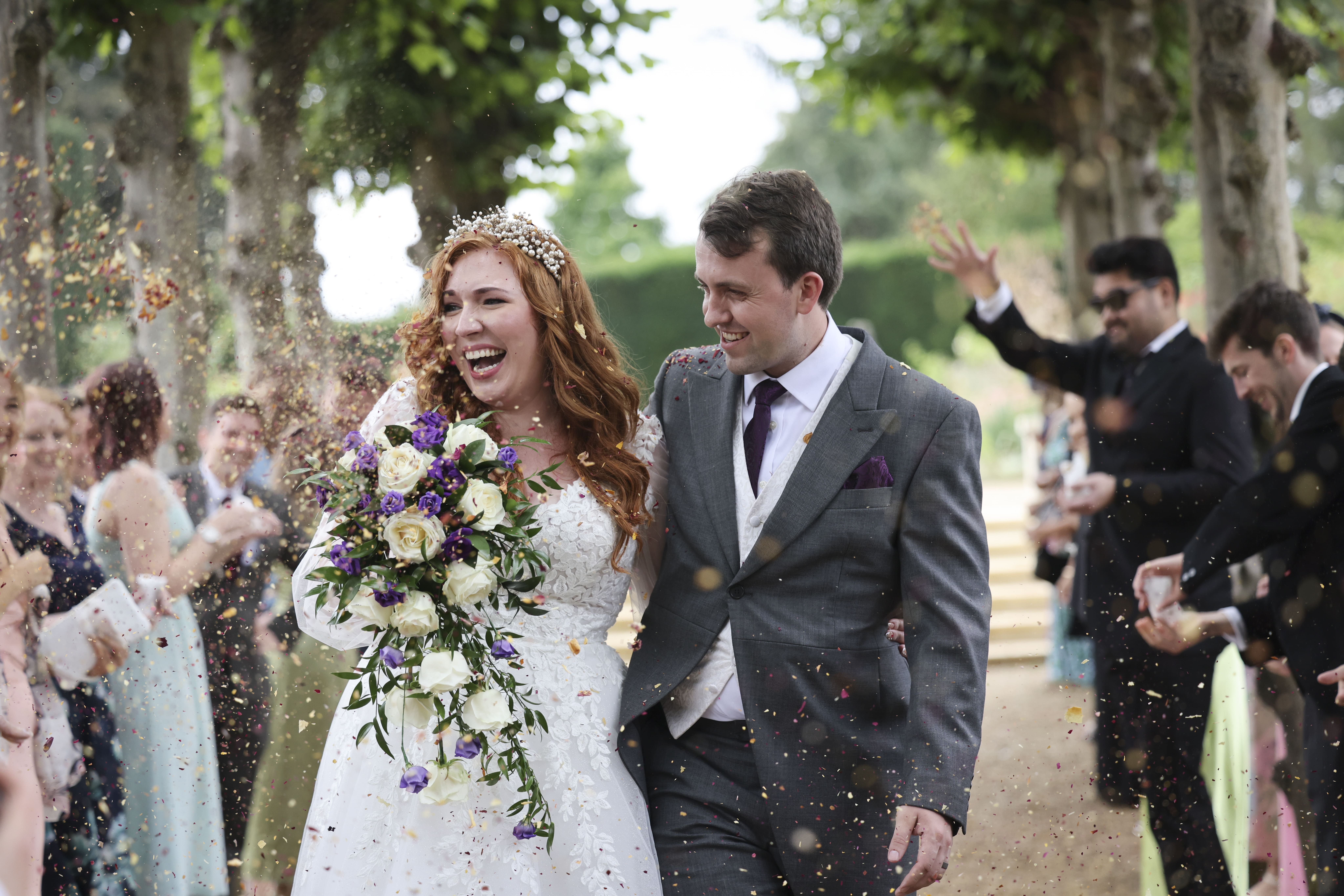 A bride and groom walking through confetti, an avenue of lime trees, Makeup By Mirna