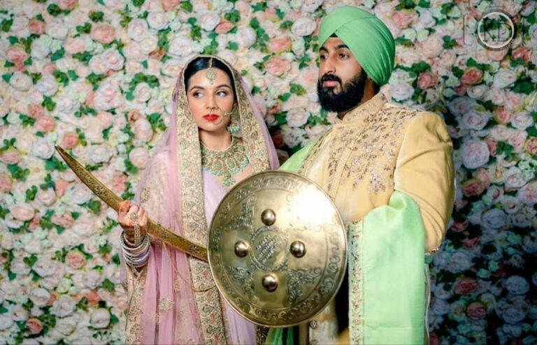 A Sikh bride and groom, ceremonial sword and shield, a floral backdrop, Makeup By Mirna