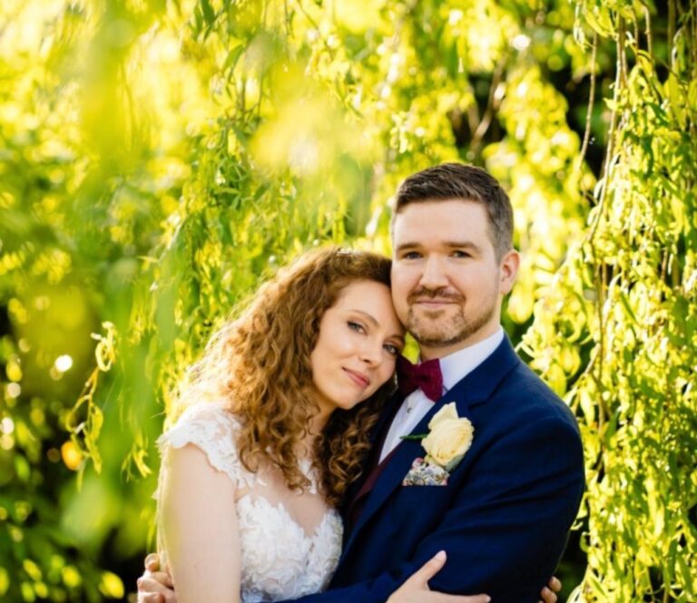 A bride and groom embracing beneath a willow tree, Makeup By Mirna