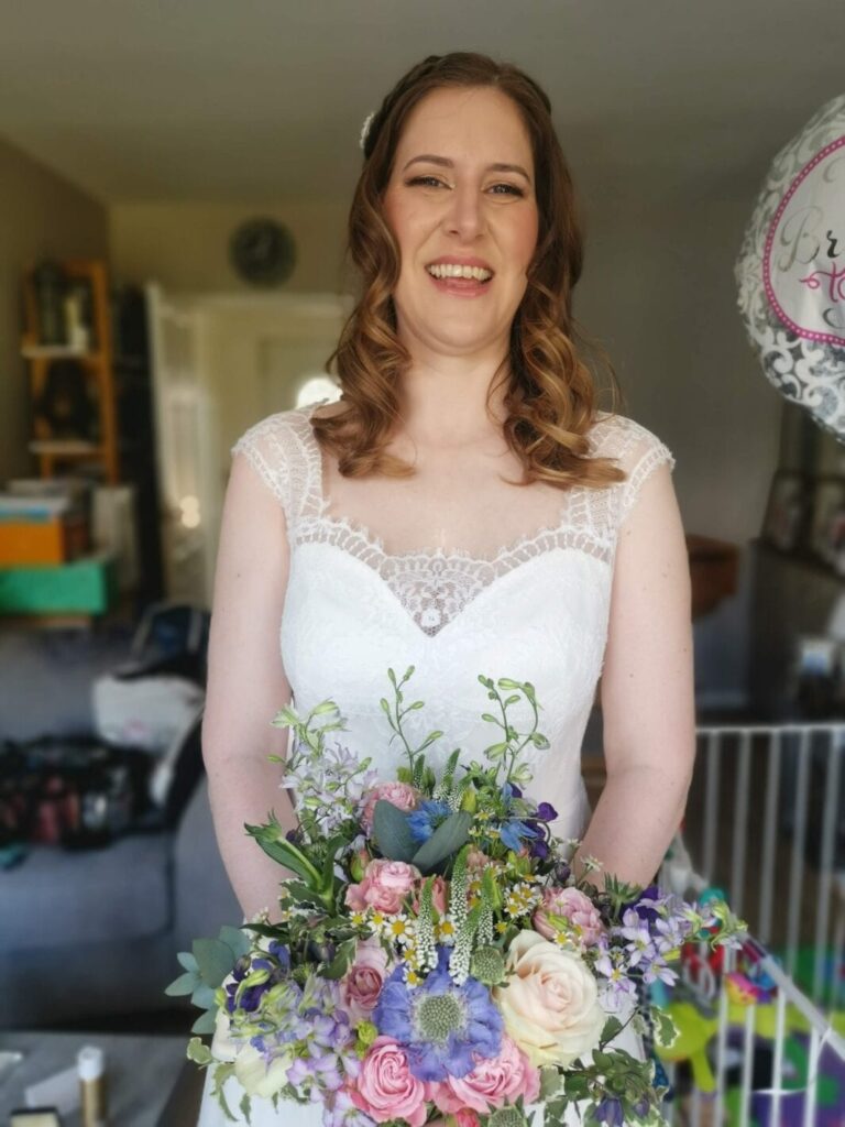 A bride at home, a mixed pastel bouquet, family photographs behind, Makeup By Mirna