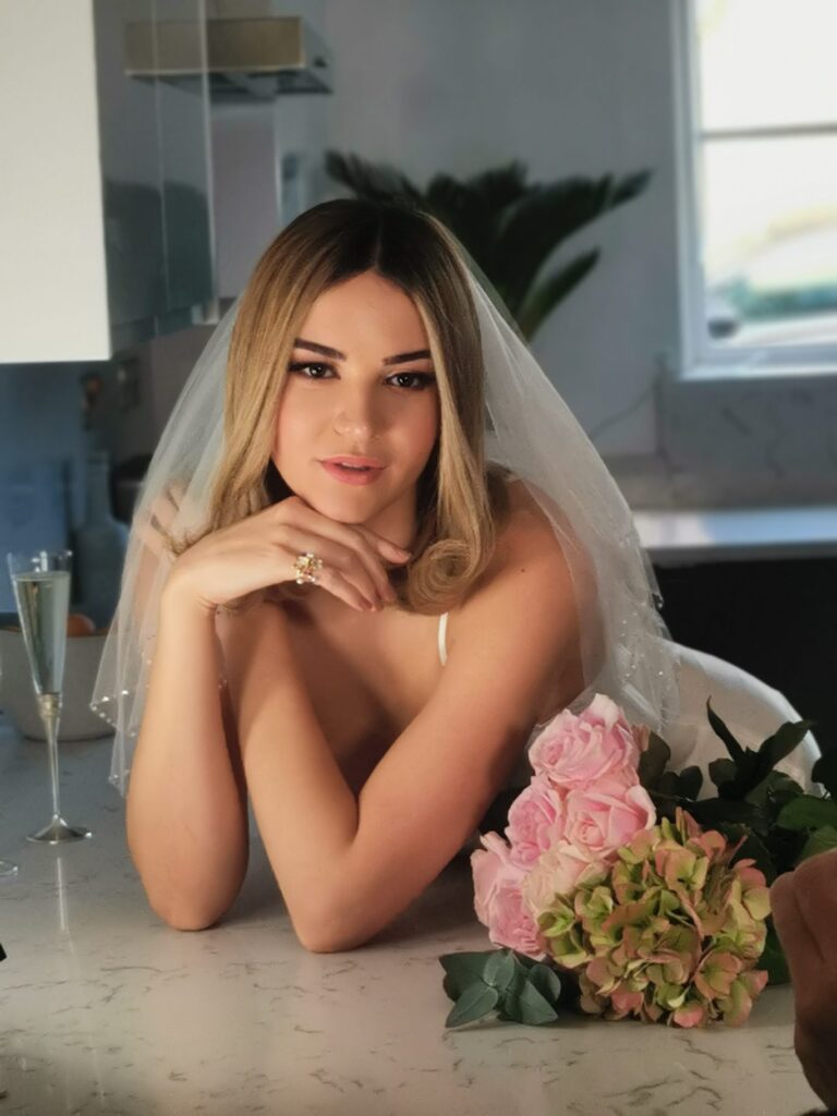A bride at the kitchen counter, a pink and green bouquet in front of her, Makeup By Mirna