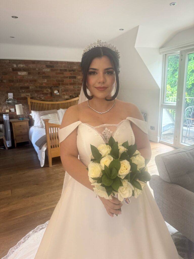A bride at home, tiara and a white rose bouquet, exposed brick behind, Makeup By Mirna