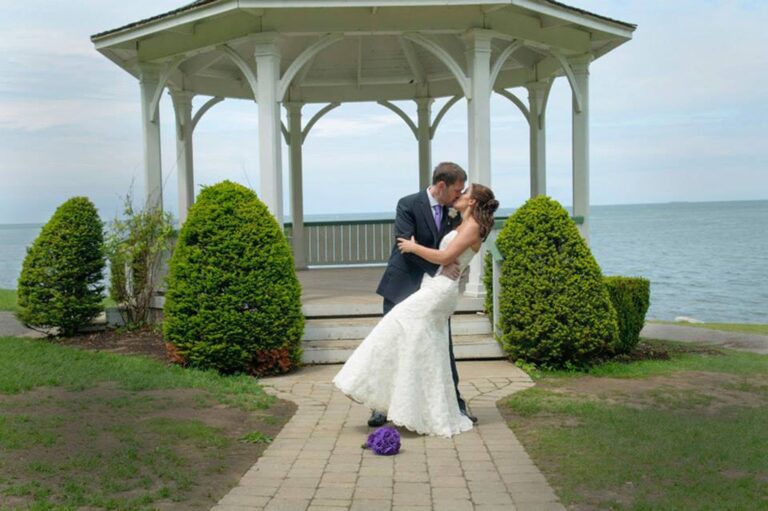A bride dipped in a kiss on the path to a white lakeside gazebo, Ontario, Maple Leaf Weddings