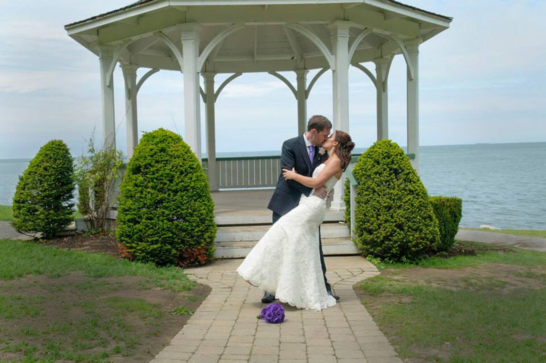 A bride dipped in a kiss on the path to a white lakeside gazebo, Ontario, Maple Leaf Weddings