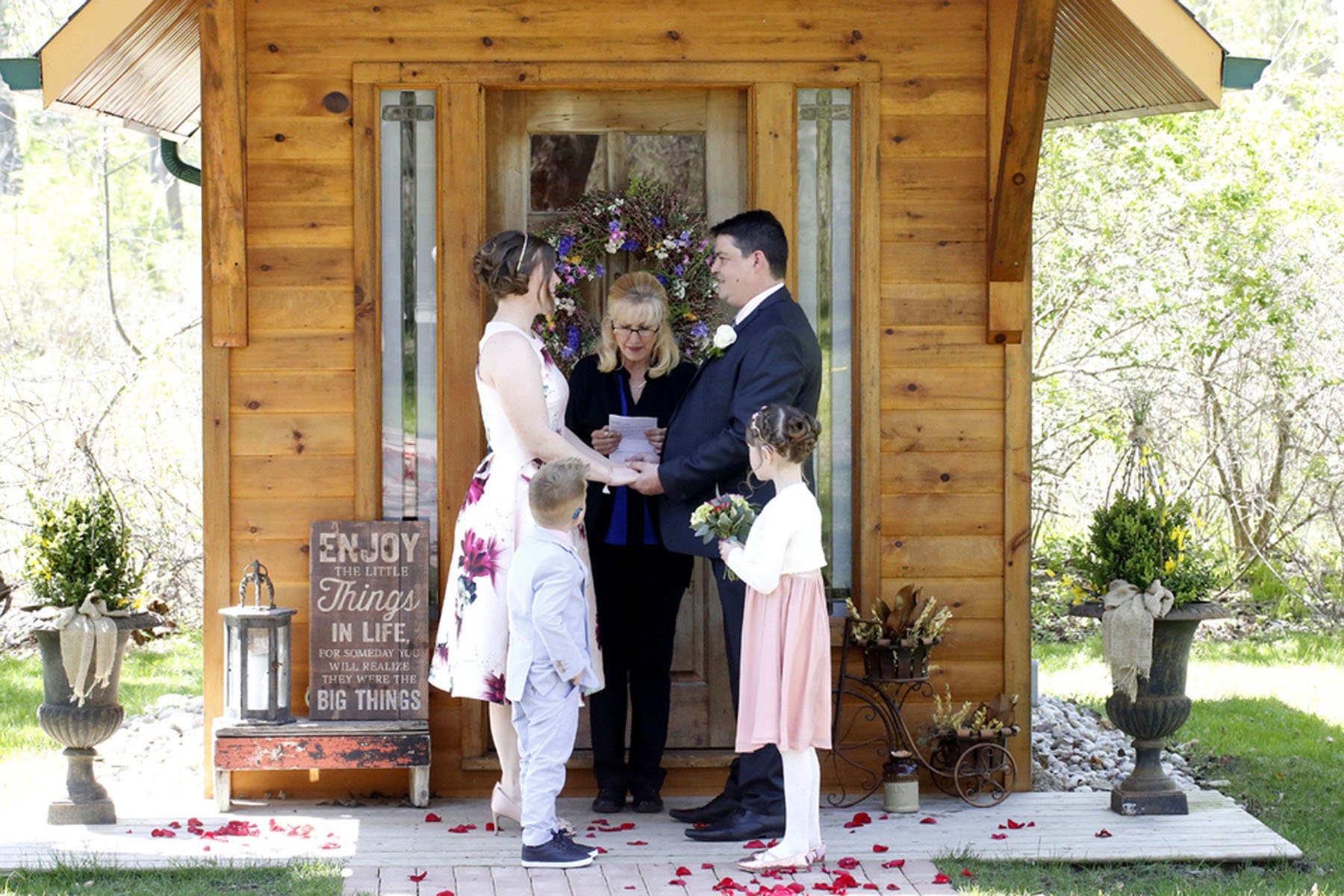 A celebrant marrying a couple on the porch of the Little Log Chapel, with two children beside them, Niagara, Maple Leaf Weddings