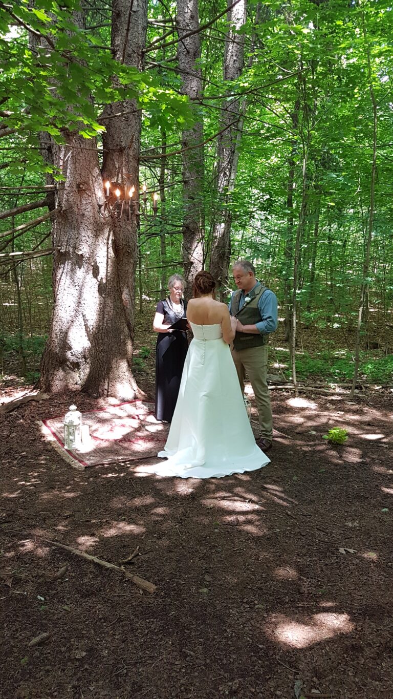 A couple saying their vows beneath tall trees in a woodland clearing, Maple Leaf Weddings