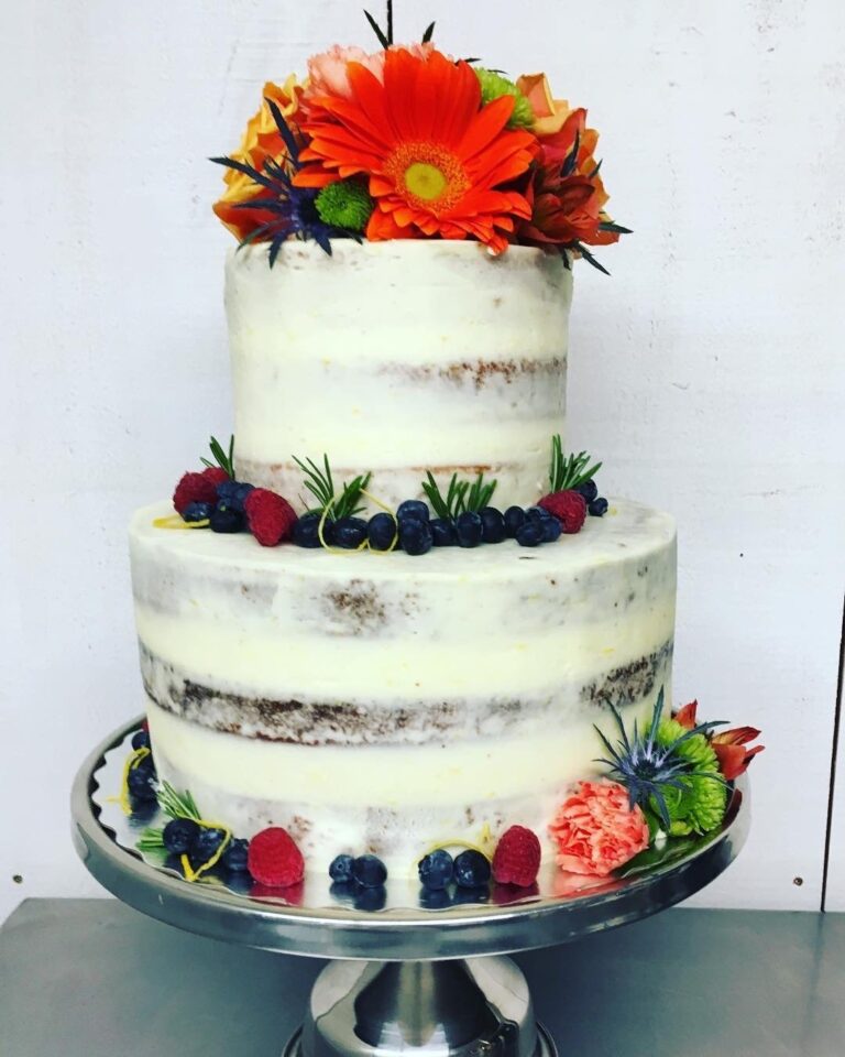 A two-tier semi-naked cake with berries and orange gerbera on a metal stand, Maple Leaf Weddings