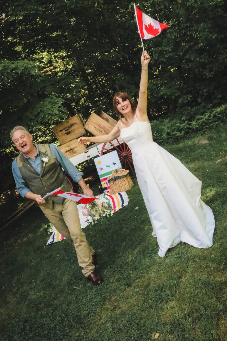 A bride and groom celebrating with a Canadian flag on the lawn after their elopement, Maple Leaf Weddings