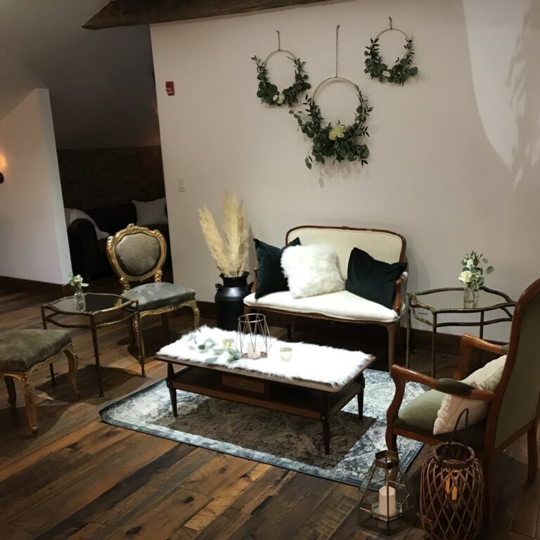 A venue lounge with vintage seating, a marble table and greenery wreaths on the wall, Maple Leaf Weddings