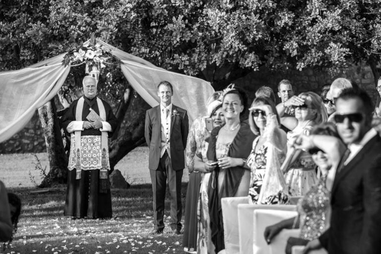 Black and white of the groom waiting at the ceremony as the priest looks on, Marco Ficili