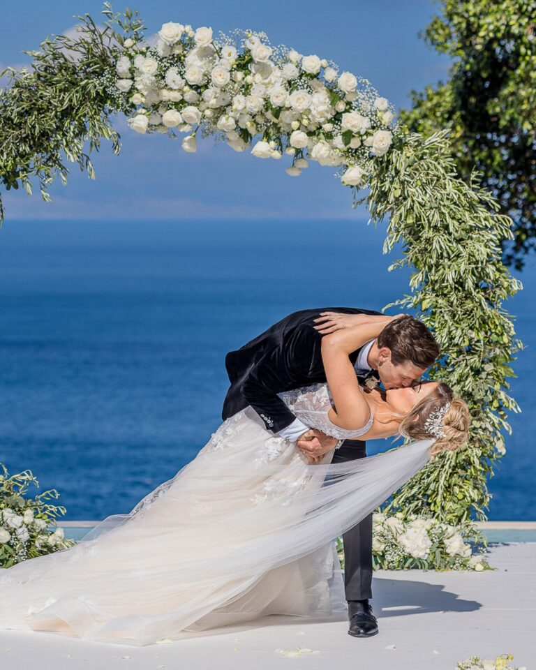 A dip kiss beneath a floral arch above the sea, Marco Ficili