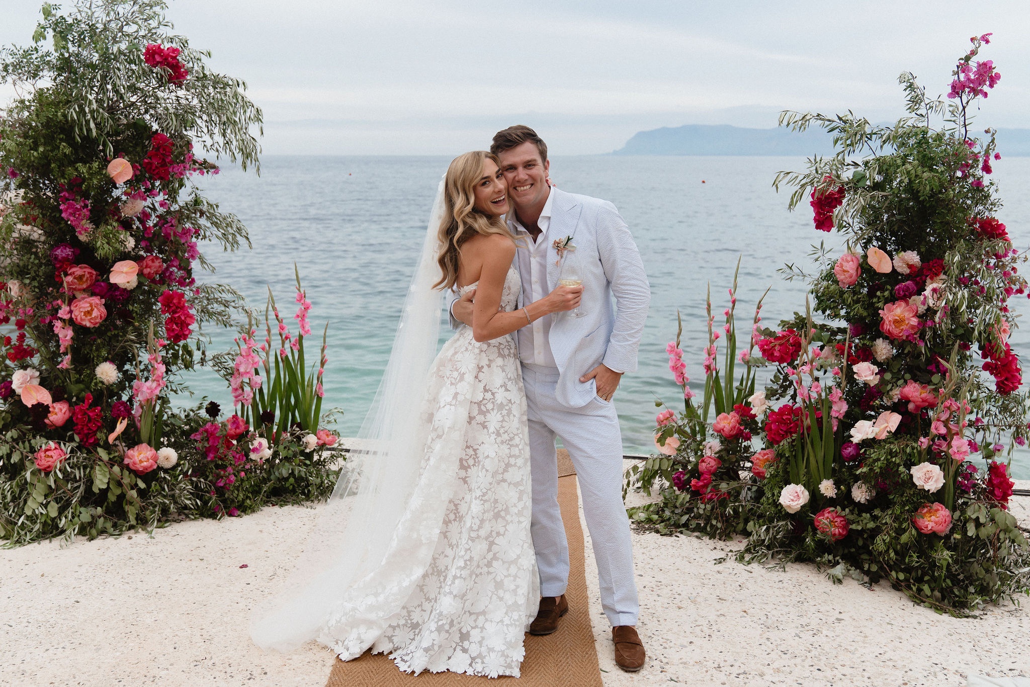 The couple on a sand aisle by the sea, between columns of coral and pink flowers, Marica Events