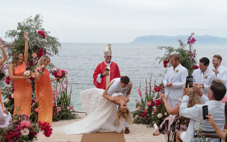 The recessional: the groom dips the bride, the celebrant in red vestments behind, Marica Events