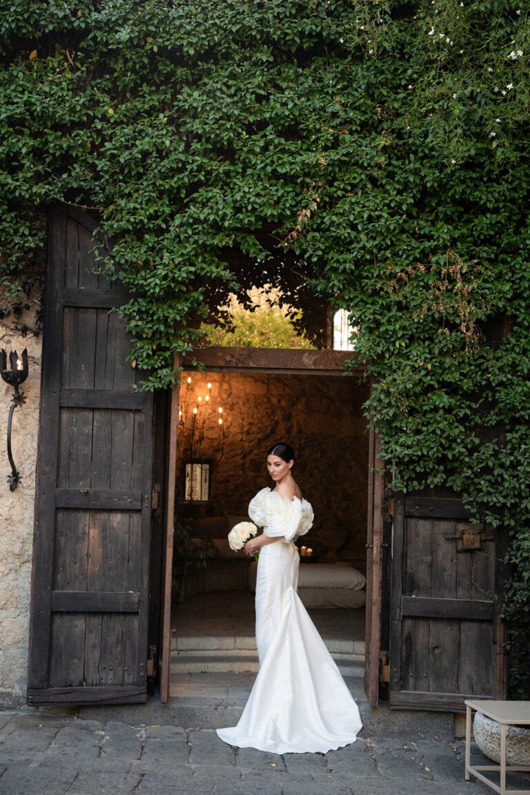A bride in the open doorway of an ivy-covered stone entrance, the doors thrown back, Marica Events