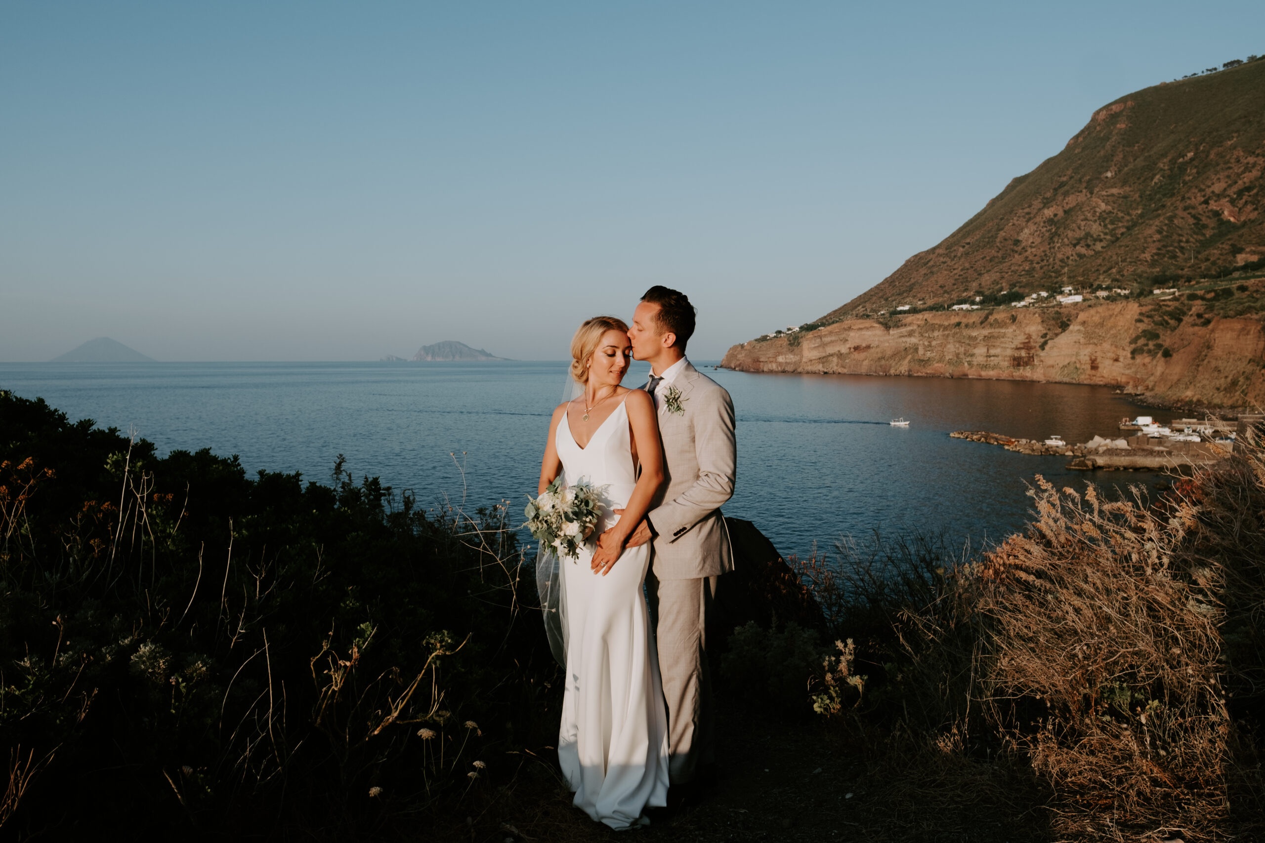 The couple on a dark hillside at dusk, a headland to one side, islands on the horizon, Marica Events