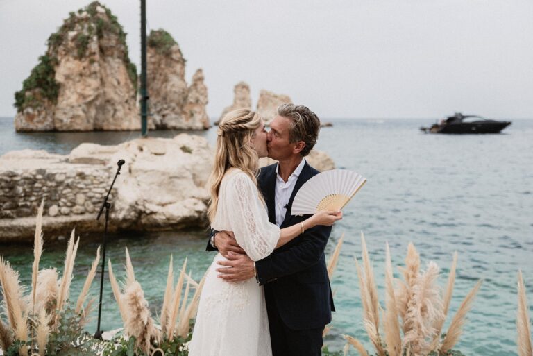 A kiss at the water's edge, rock stacks behind them and a motor yacht offshore, Marica Events