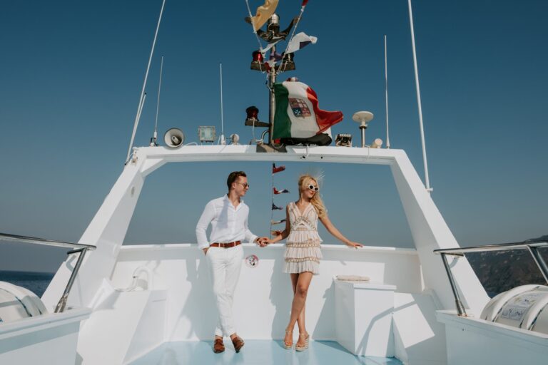 The couple on the foredeck of a white motor yacht, the Italian flag flying above, Marica Events