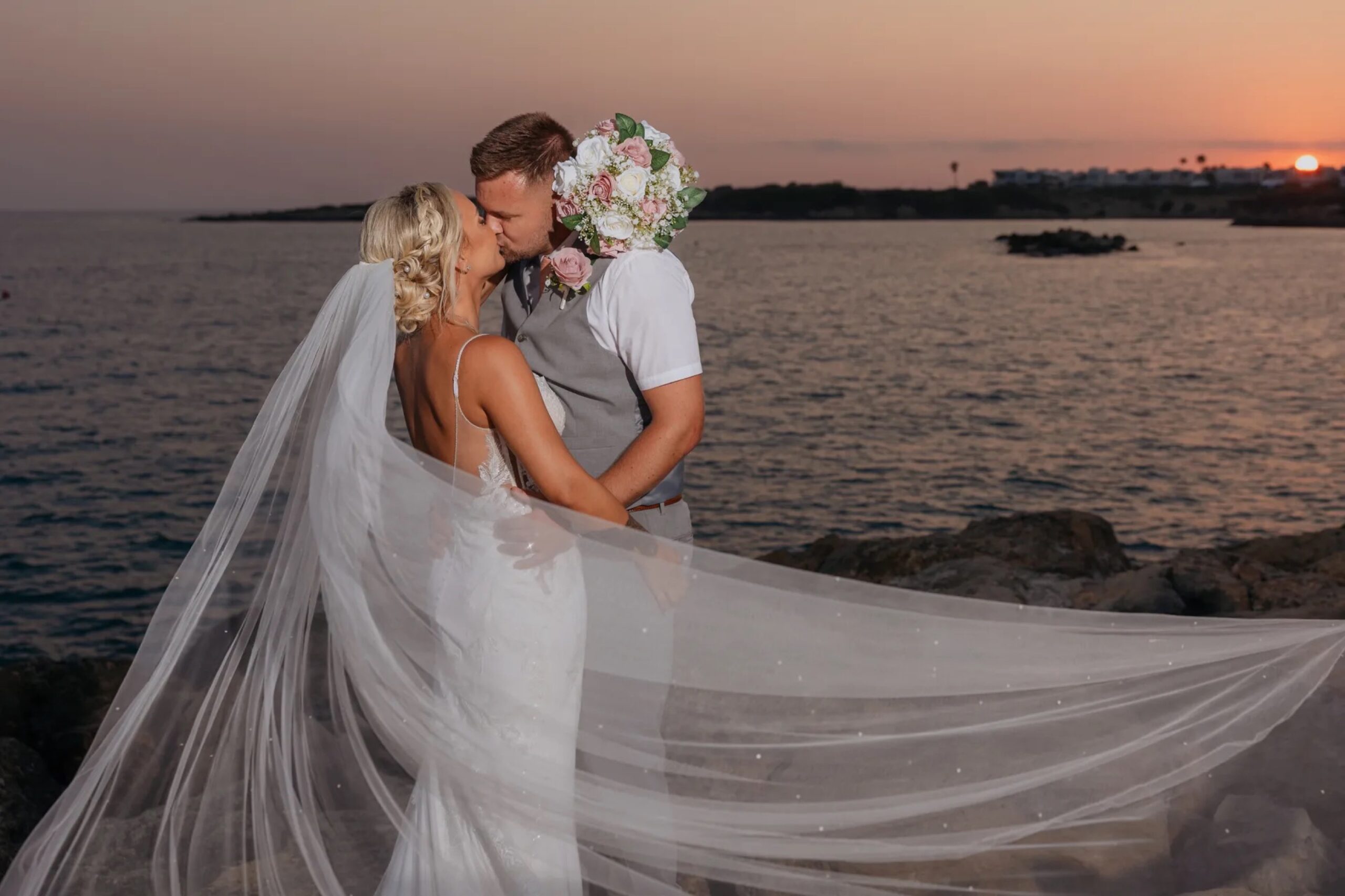 Couple kissing at sunset with a long veil on the rocks at Coral Beach, Paphos, Marry Me Cyprus