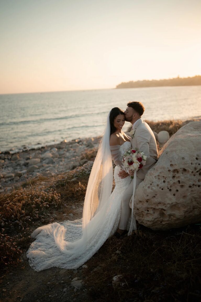 Couple on a rocky shore at sunset, veil lifting in the wind, Coral Bay, Paphos, Marry Me Cyprus