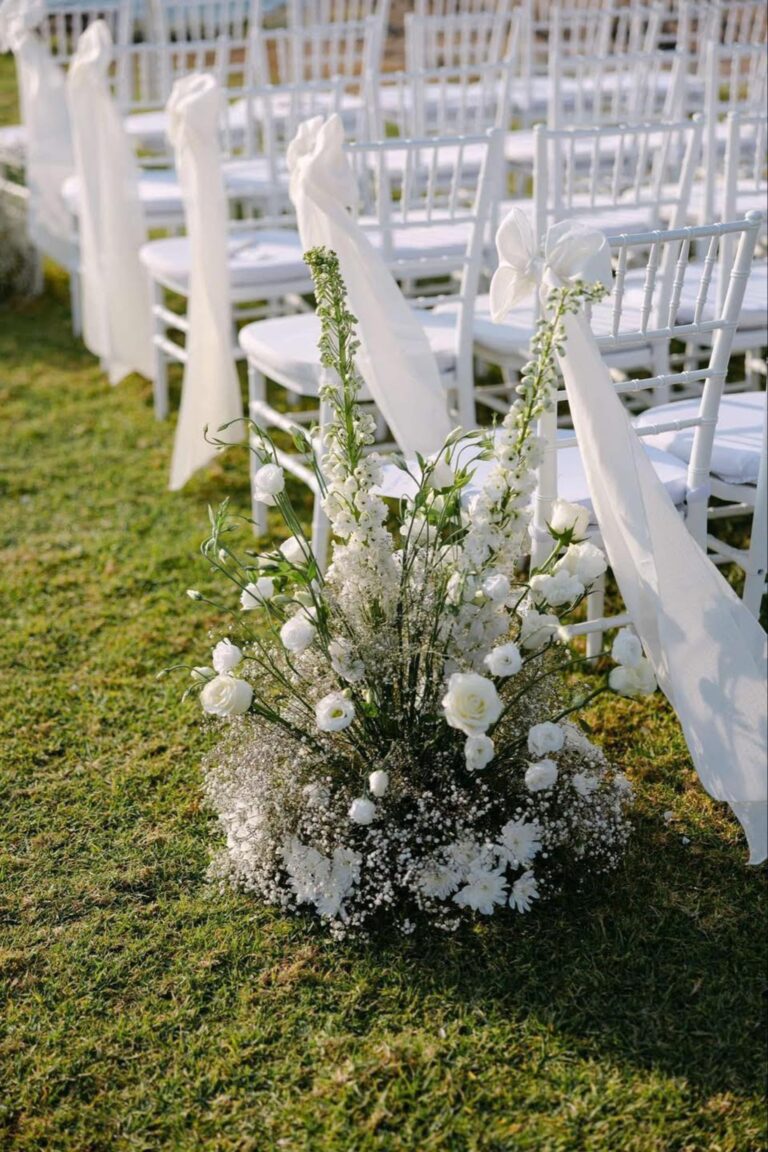 White chairs with ribbons and flower clusters on the ceremony lawn at Alassos, Paphos, Marry Me Cyprus