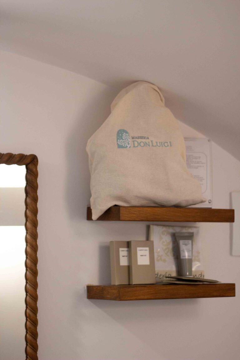 Wooden shelves with a masseria tote bag and toiletries beside a twisted wooden mirror frame, Masseria Don Luigi